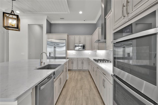 kitchen with light stone countertops, wall chimney exhaust hood, stainless steel appliances, sink, and pendant lighting