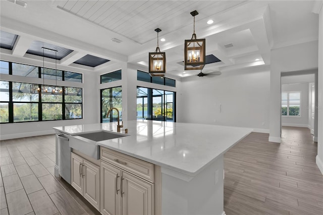 kitchen featuring light stone countertops, a kitchen island with sink, sink, decorative light fixtures, and light hardwood / wood-style flooring