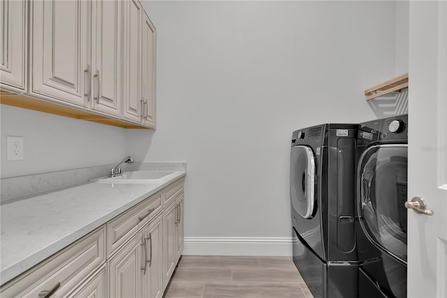 laundry room featuring sink, light hardwood / wood-style flooring, cabinets, and independent washer and dryer