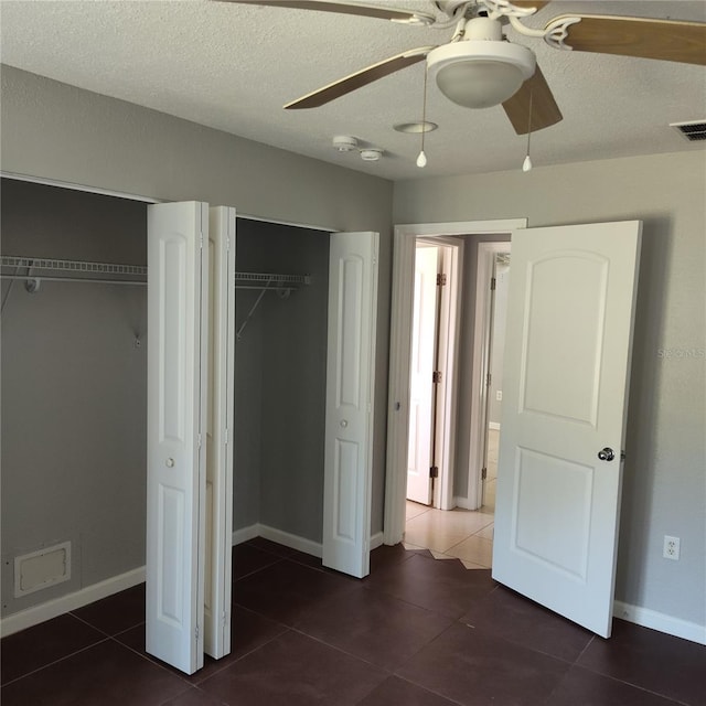 unfurnished bedroom with ceiling fan, dark tile patterned floors, a textured ceiling, and two closets