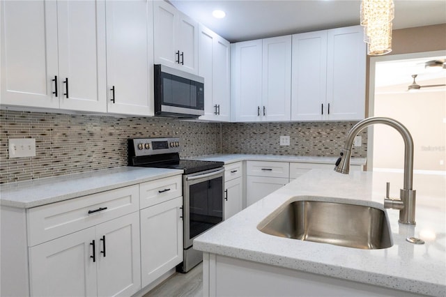 kitchen with decorative backsplash, stainless steel appliances, sink, white cabinets, and hanging light fixtures