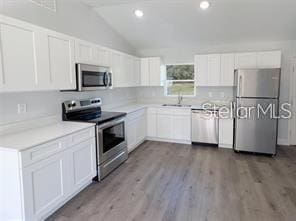 kitchen with sink, vaulted ceiling, appliances with stainless steel finishes, light hardwood / wood-style floors, and white cabinetry