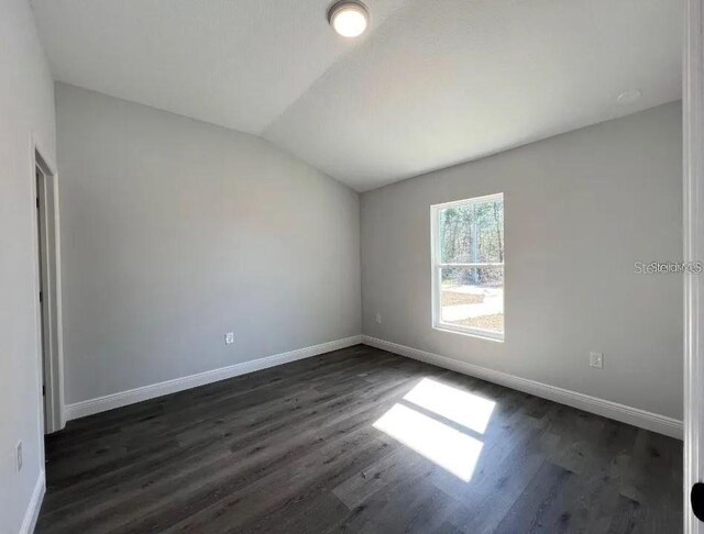 unfurnished room featuring dark wood-type flooring and vaulted ceiling