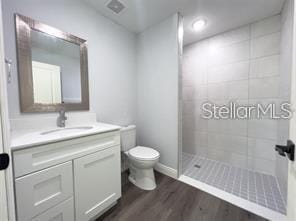 bathroom with tiled shower, hardwood / wood-style floors, vanity, and toilet