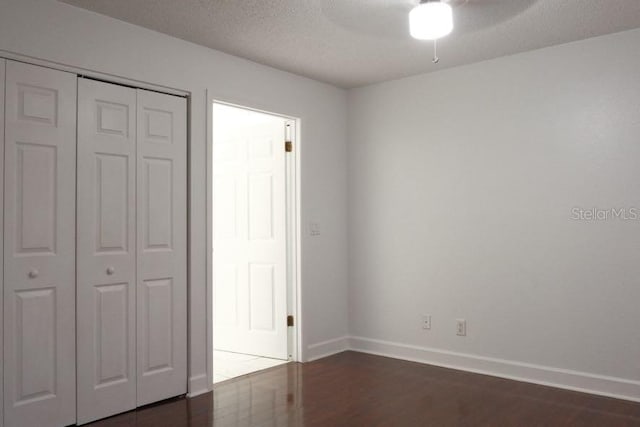 unfurnished bedroom featuring ceiling fan, dark wood-type flooring, a textured ceiling, and a closet