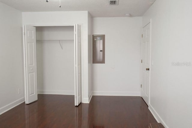 unfurnished bedroom with a closet, electric panel, dark hardwood / wood-style floors, and a textured ceiling