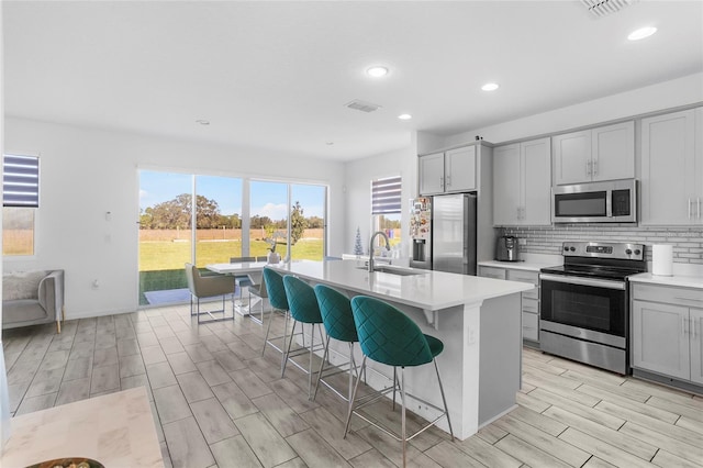 kitchen featuring sink, light hardwood / wood-style flooring, an island with sink, gray cabinets, and appliances with stainless steel finishes