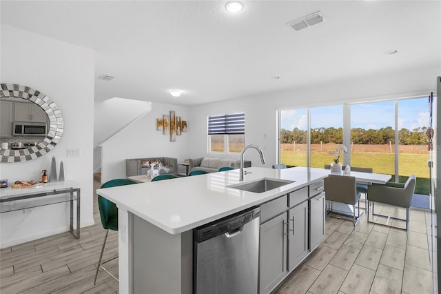 kitchen featuring gray cabinetry, stainless steel appliances, sink, light hardwood / wood-style floors, and an island with sink