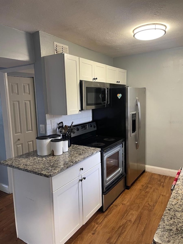 kitchen with dark stone countertops, dark hardwood / wood-style flooring, white cabinets, and stainless steel appliances