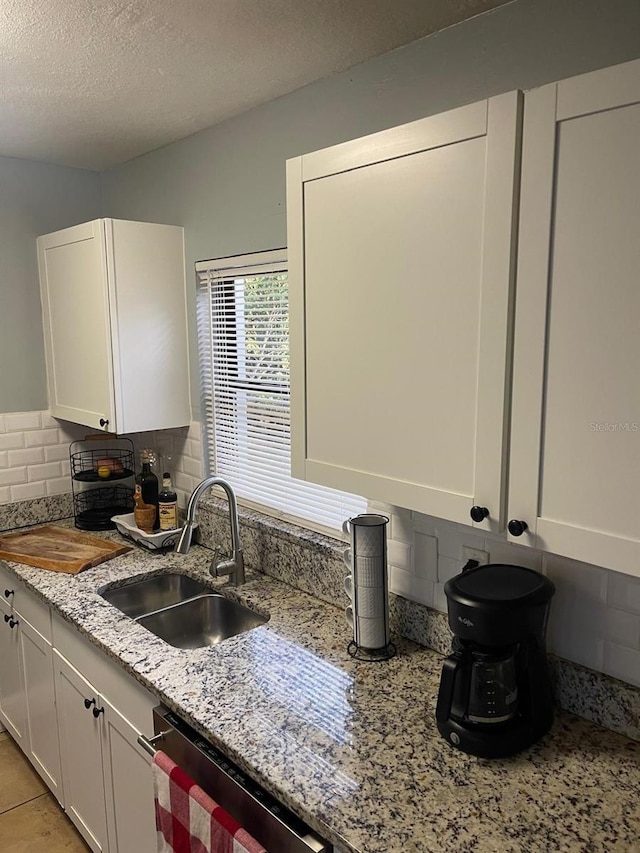 kitchen featuring light stone counters, stainless steel dishwasher, a textured ceiling, sink, and white cabinetry