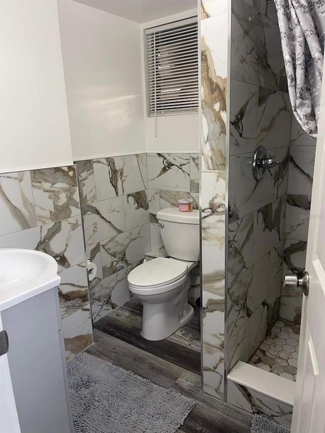 bathroom featuring toilet, wood-type flooring, a tile shower, and tile walls