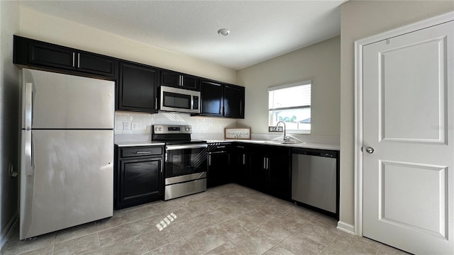 kitchen featuring sink, backsplash, a textured ceiling, light tile patterned floors, and appliances with stainless steel finishes