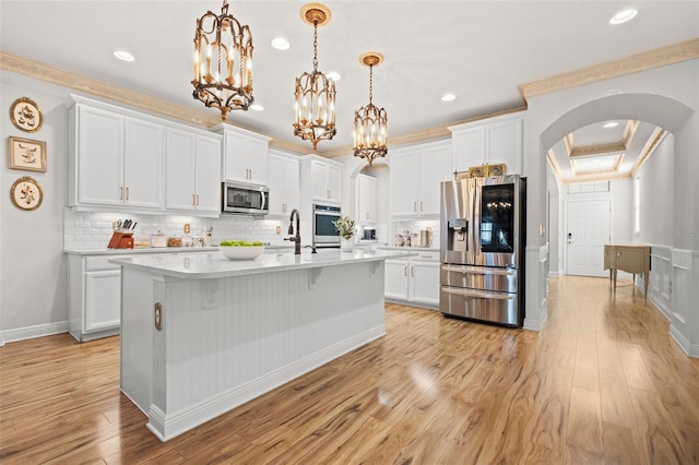 kitchen with white cabinets, hanging light fixtures, appliances with stainless steel finishes, and ornamental molding