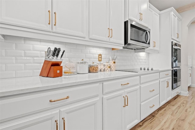 kitchen featuring light stone countertops, white cabinetry, stainless steel appliances, decorative backsplash, and light hardwood / wood-style flooring