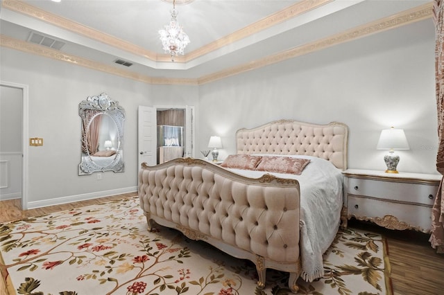 bedroom with hardwood / wood-style flooring, a tray ceiling, crown molding, and a chandelier