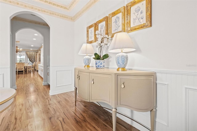 hallway featuring light wood-type flooring, an inviting chandelier, and ornamental molding