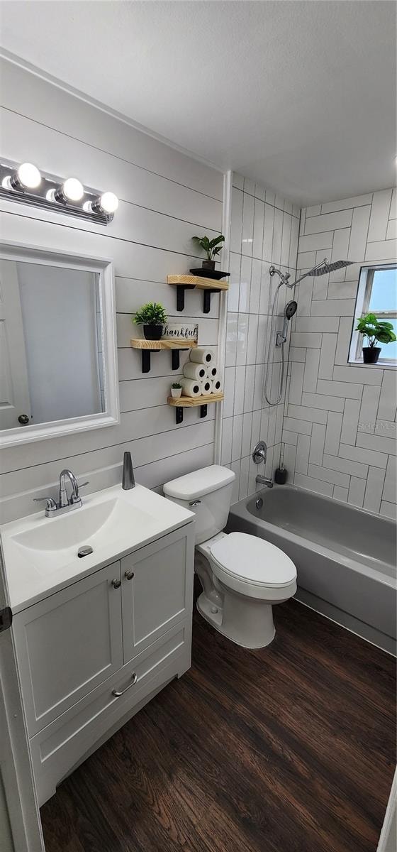 full bathroom with tiled shower / bath, toilet, wooden walls, vanity, and hardwood / wood-style flooring