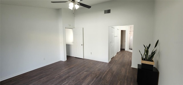 empty room with a towering ceiling, ceiling fan, and dark wood-type flooring