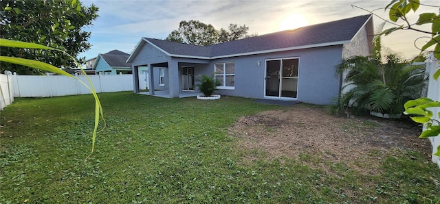 back house at dusk featuring a yard and a patio