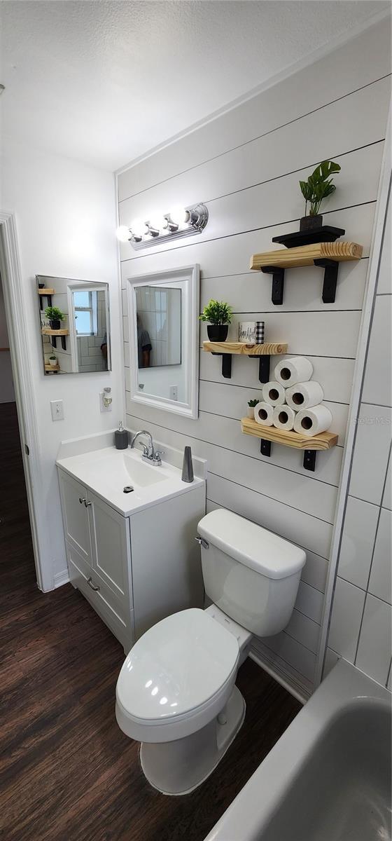 bathroom with a washtub, wood-type flooring, toilet, wooden walls, and vanity