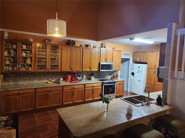 kitchen featuring stainless steel appliances, sink, decorative light fixtures, a high ceiling, and a breakfast bar area