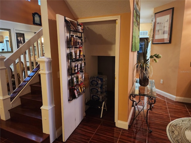 hallway featuring lofted ceiling, dark tile patterned flooring, and a textured ceiling