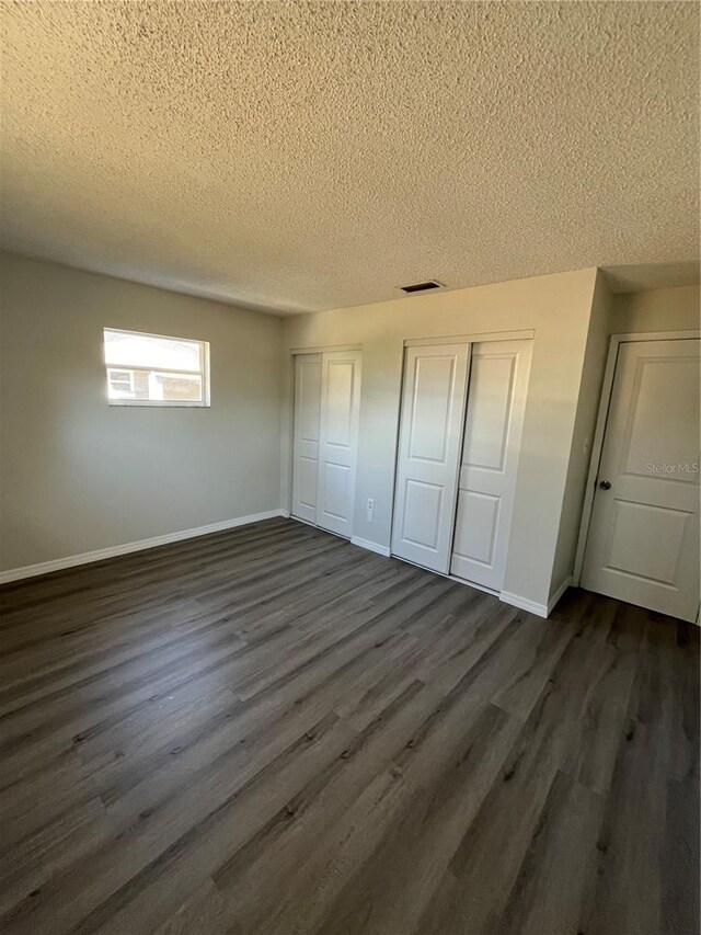 unfurnished bedroom with dark hardwood / wood-style floors, a textured ceiling, and multiple closets