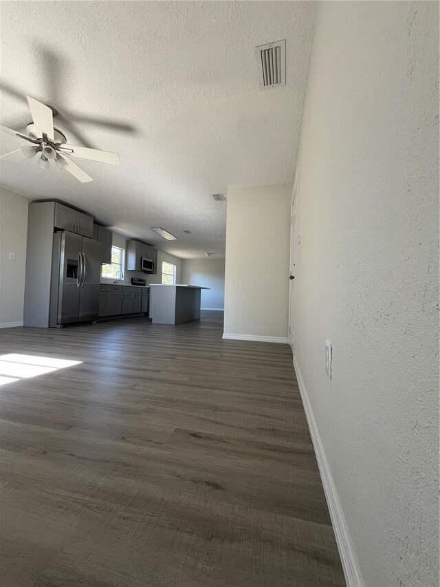 unfurnished living room with a textured ceiling, ceiling fan, and dark wood-type flooring