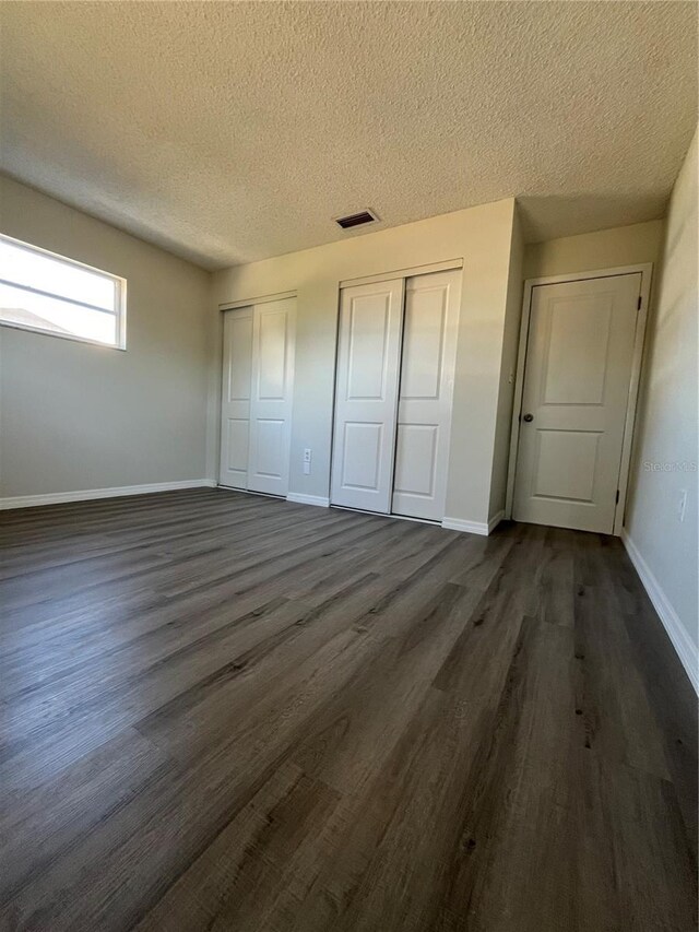 unfurnished bedroom featuring dark hardwood / wood-style floors, a textured ceiling, and two closets