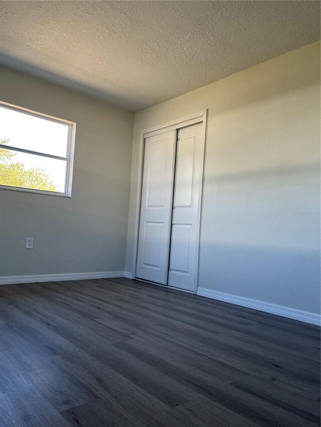 unfurnished bedroom featuring a textured ceiling, a closet, and dark wood-type flooring