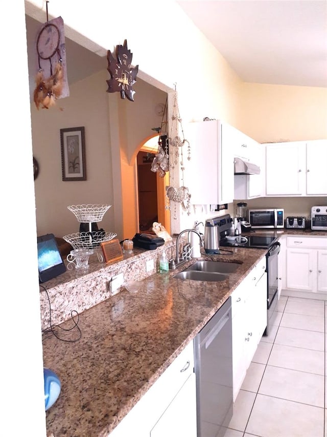 kitchen featuring appliances with stainless steel finishes, dark stone counters, sink, white cabinets, and light tile patterned flooring