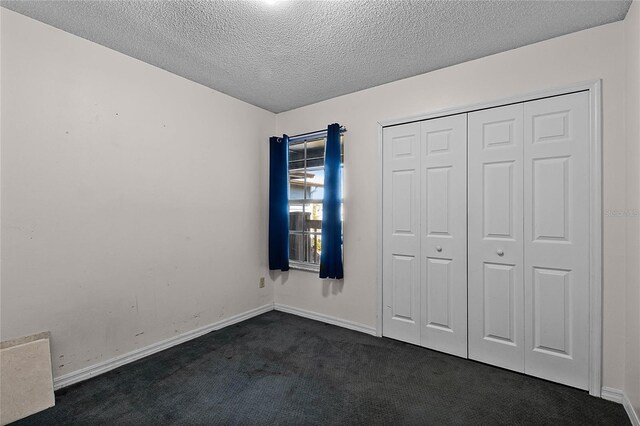 unfurnished bedroom with dark carpet, a textured ceiling, and a closet