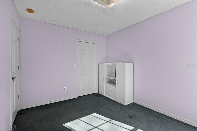 unfurnished bedroom featuring a closet, dark carpet, and a textured ceiling