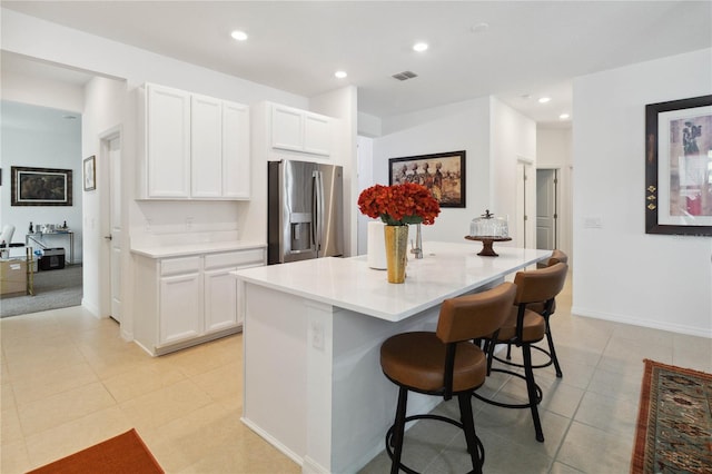 kitchen featuring a kitchen breakfast bar, white cabinetry, stainless steel refrigerator with ice dispenser, and a kitchen island with sink