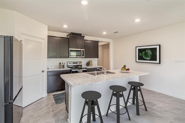 kitchen with appliances with stainless steel finishes, dark brown cabinets, a kitchen island with sink, sink, and a breakfast bar area