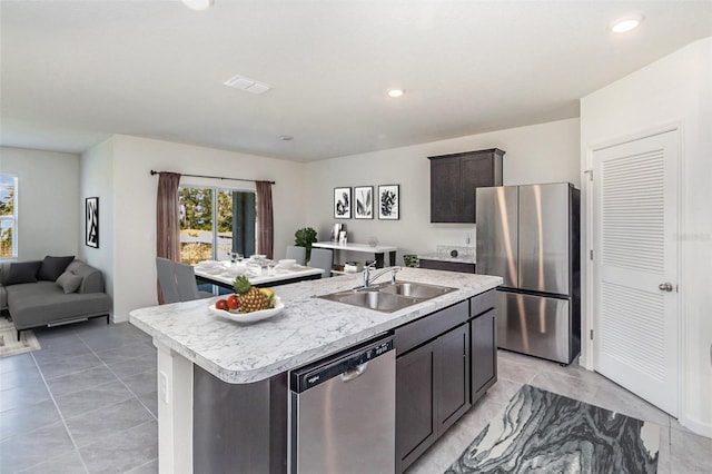 kitchen with sink, light tile patterned floors, stainless steel appliances, and a kitchen island with sink