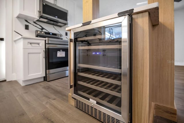 kitchen featuring beverage cooler, light wood-type flooring, white cabinetry, and appliances with stainless steel finishes