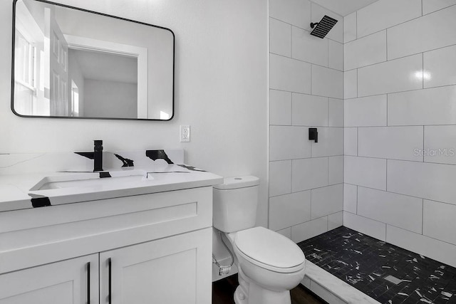 bathroom with vanity, toilet, and tiled shower