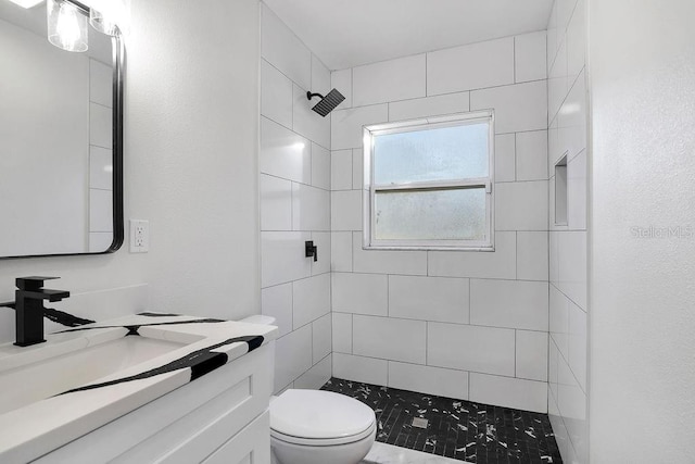 bathroom featuring a tile shower, vanity, and toilet