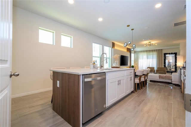 kitchen featuring stainless steel dishwasher, sink, white cabinetry, hanging light fixtures, and an island with sink