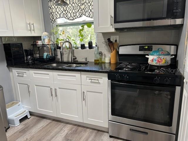 kitchen featuring backsplash, stainless steel appliances, sink, light hardwood / wood-style floors, and white cabinetry