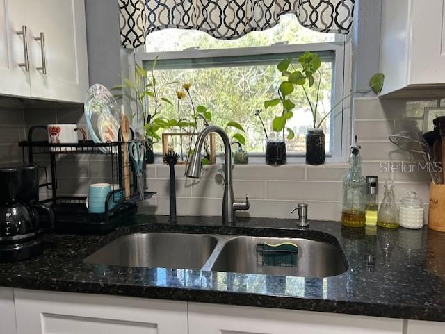 kitchen featuring white cabinets, decorative backsplash, dark stone counters, and sink