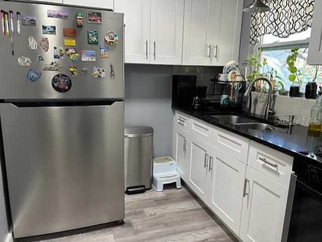 kitchen featuring light wood-type flooring, sink, white cabinets, oven, and stainless steel refrigerator