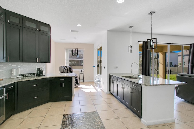 kitchen with tasteful backsplash, light stone counters, sink, light tile patterned floors, and hanging light fixtures