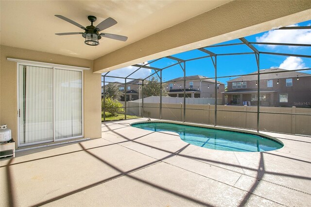 view of swimming pool featuring glass enclosure, ceiling fan, and a patio area