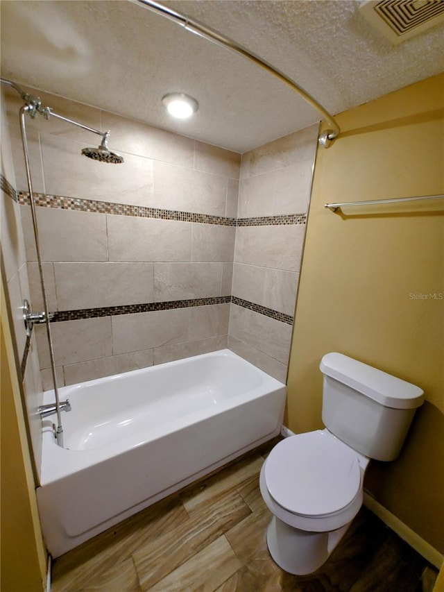 bathroom with a textured ceiling, tiled shower / bath combo, and toilet