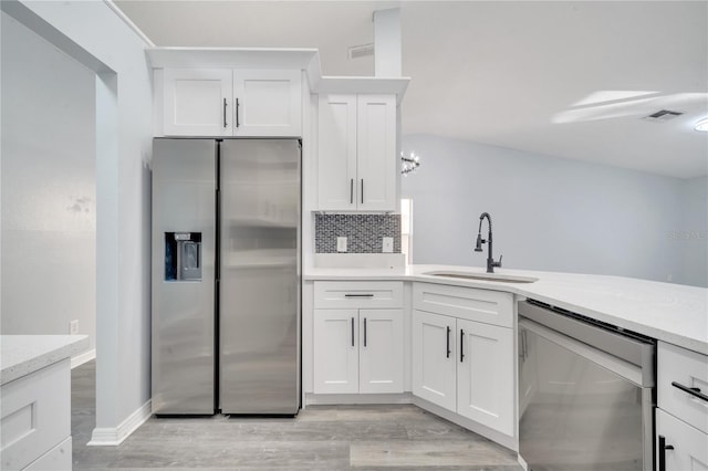 kitchen featuring appliances with stainless steel finishes, tasteful backsplash, sink, white cabinets, and light hardwood / wood-style floors