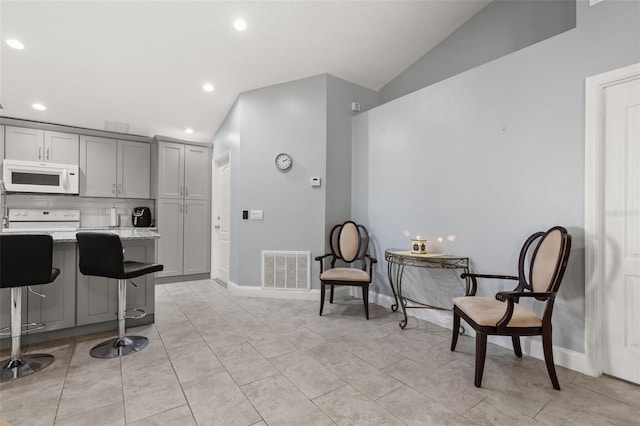 kitchen featuring gray cabinetry, light stone countertops, white appliances, and vaulted ceiling