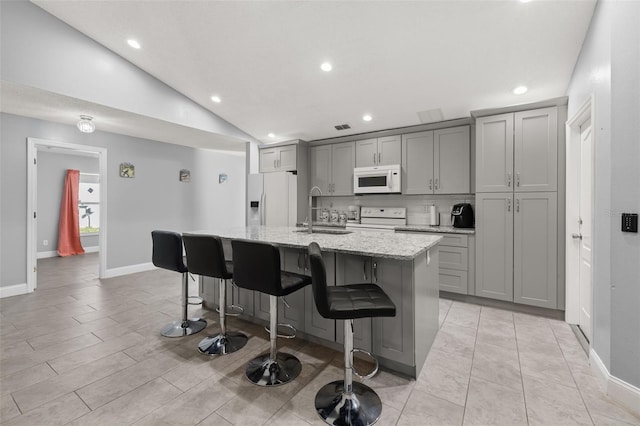 kitchen with a center island with sink, gray cabinets, white appliances, and vaulted ceiling