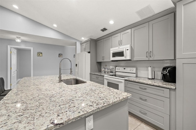 kitchen with white appliances, light stone counters, vaulted ceiling, and sink